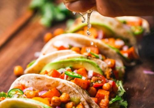 A hand squeezes lime juice over a row of tacos filled with chickpeas, avocado, and veggies, garnished with cilantro on a wooden board.