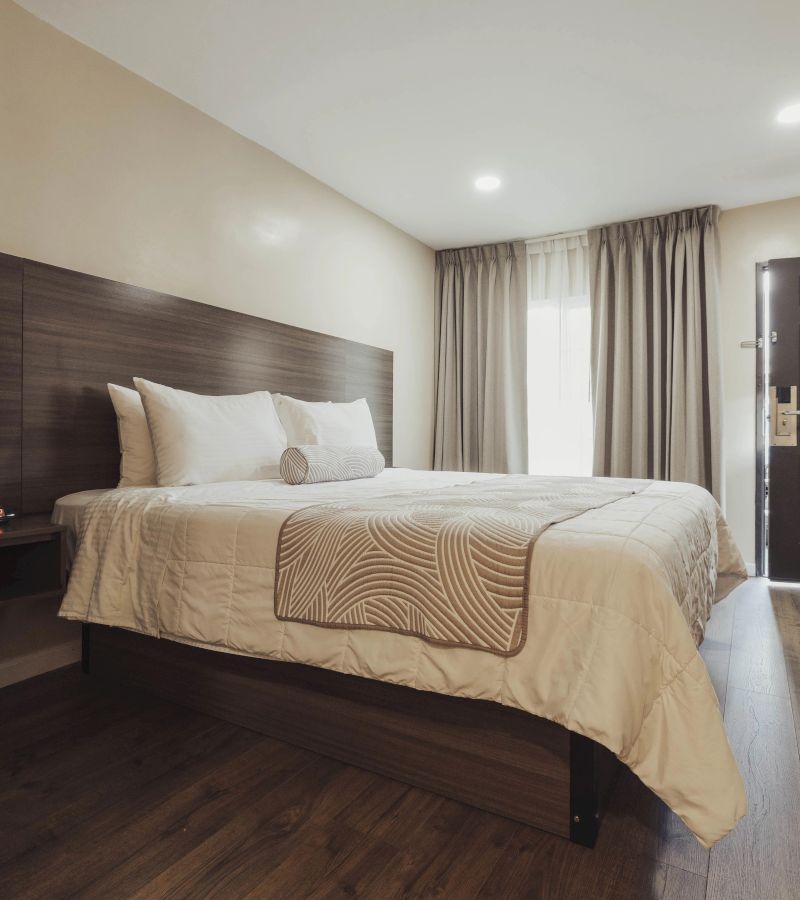 A wide view of a hotel room with a large bed, window, and door.