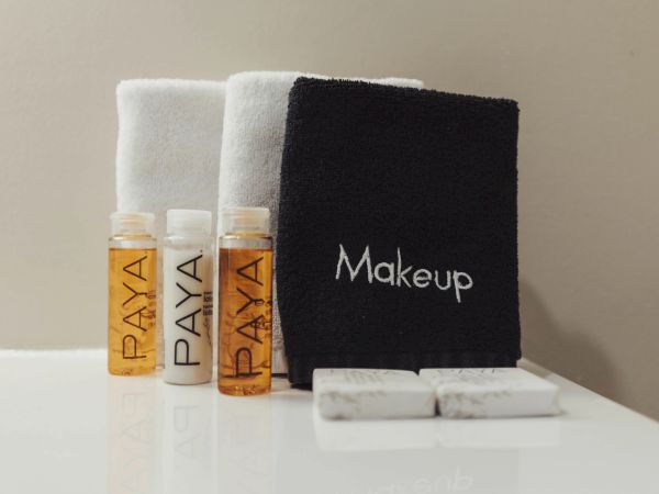 The image shows two white towels, a black makeup towel, and three bottles labeled "Paya" on a counter.