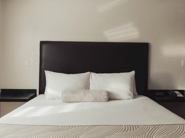A neatly made bed with white linens, two pillows, and a bolster pillow, flanked by two side tables with a phone on one.