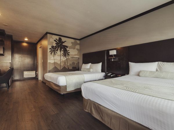 A modern hotel room with two beds, wood flooring, palm tree mural, desk, and chair, creating a cozy and stylish environment.