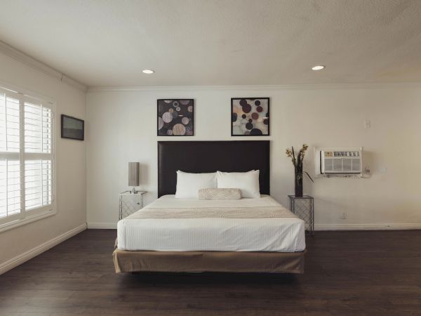 A modern bedroom with a neatly made bed, two artworks above the headboard, and an air conditioning unit on the wall.