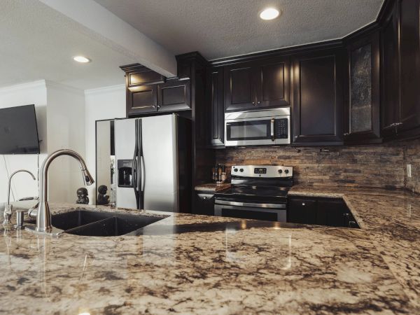 The image shows a modern kitchen with dark cabinets, stainless steel appliances, and granite countertops.