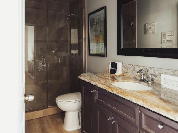 A bathroom with a granite countertop, under-mount sink, toilet, and glass-enclosed shower; decorated with a framed picture and mirror.