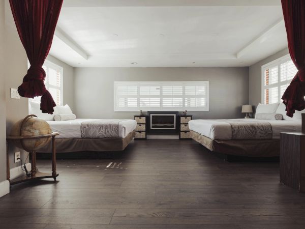 The image shows a spacious bedroom with two beds, a globe, and a fireplace, flanked by windows with red curtains.