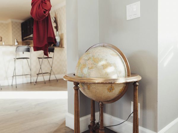 A vintage globe on a wooden stand is placed in a room with wooden flooring and red curtains.