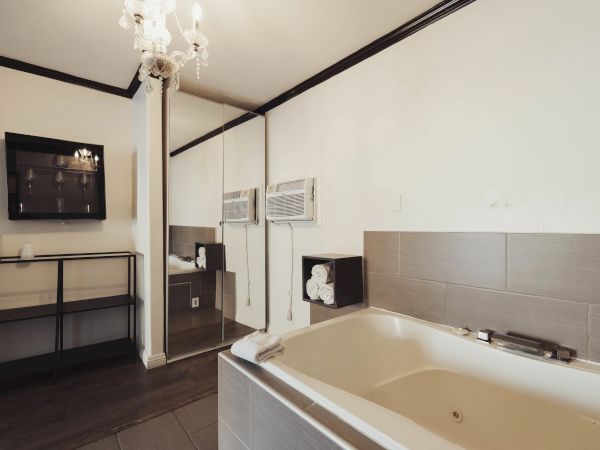 A bathroom with a bathtub, mirrored wall, shelves, and a chandelier creates a modern and elegant atmosphere.