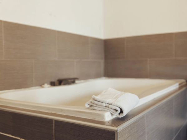 A bathroom with a tiled bathtub and folded white towels placed on its edge.