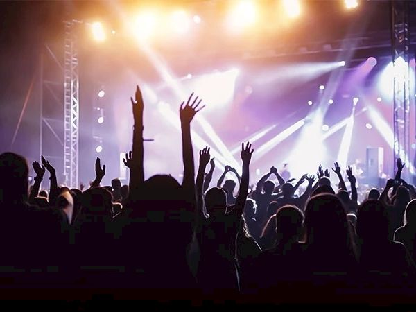 A crowd of people with raised hands enjoying a concert, illuminated by vibrant stage lights.