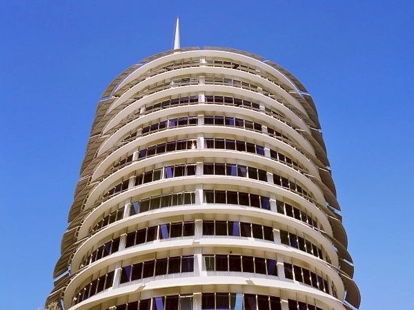 The image shows a circular, multi-level building with a distinctive layered design against a clear blue sky.