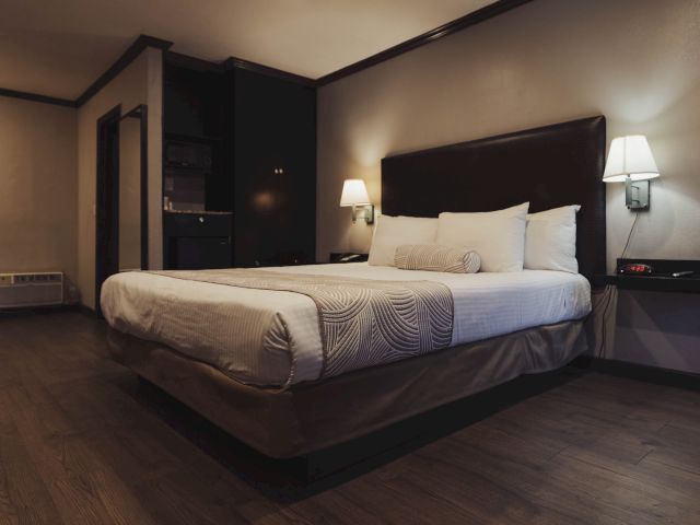 A wide-angle view of a hotel room with a large bed, two lamps, and a built-in cabinet.