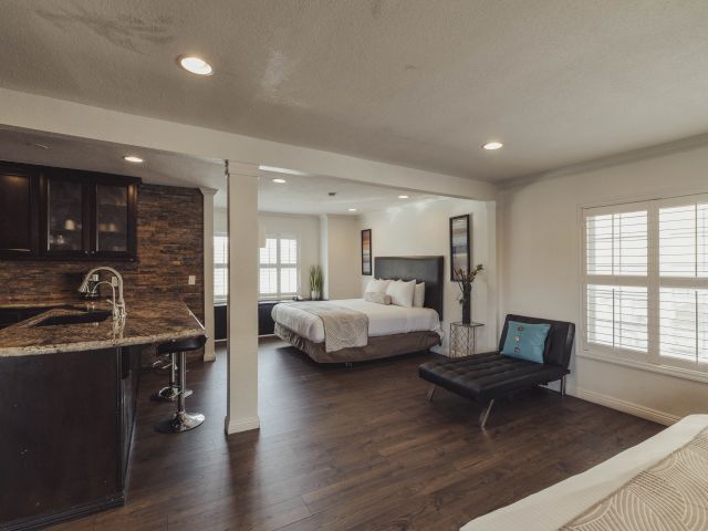 A wide view of a hotel suite with a kitchenette, bed, and sofa.