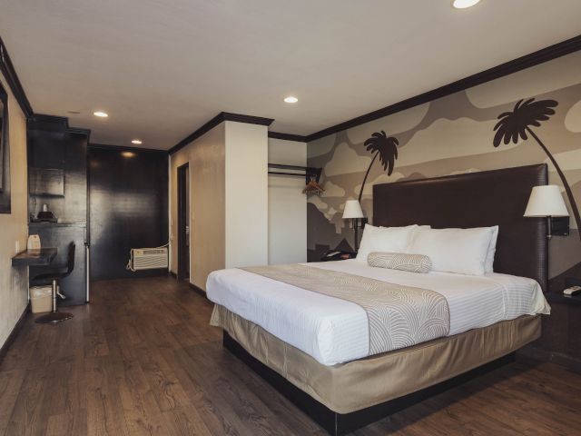 A wide-angle view of a hotel room with a large bed, desk, and door.