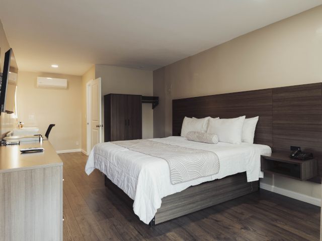 A wide view of a hotel room with a large bed, desk, wardrobe, and TV.