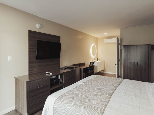 A wide-angle view of a hotel room with a bed, TV, desk, and wardrobe.