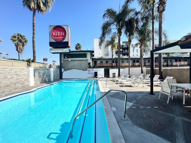 A swimming pool with a sign in the background and lounge chairs and palm trees around it.