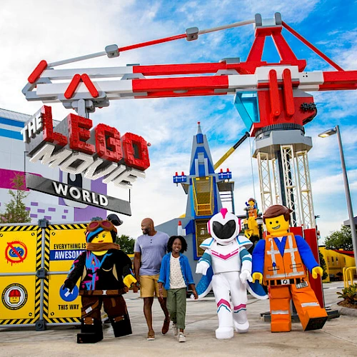 People with LEGO character mascots pose at "The LEGO Movie World" entrance in a theme park setting.